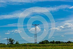 High voltage power lines on blue sky with few white clouds in the field