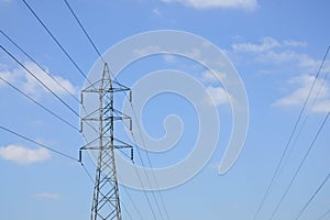 High voltage power lines with electricity pylons at blue sky.