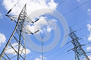 High voltage power lines with electricity pylons at blue sky.