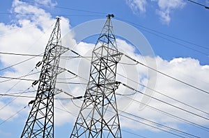 High voltage power lines with electricity pylons at blue sky.