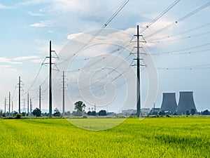 High voltage power lines. In foreground green fields, in background the cooling towers of a large power plant.