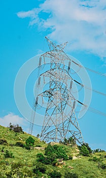High voltage power lines leading through a green field . Transmission of electricity by means of supports through hilly areas.