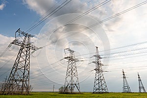 High-voltage power lines passing through a green field, on the background of a beautiful cloudy sky