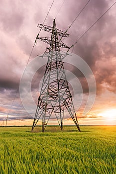 High-voltage power lines passing through a green field, on the background of a beautiful cloudy sky