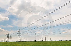 High-voltage power lines passing through a green field, on the background of a beautiful cloudy sky