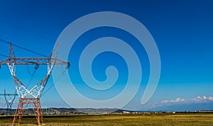 High voltage power lines on power pylons on a large grass field