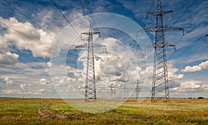 High voltage power lines in steppe covered with green and yellow grass under deep blue sky with heavy clouds.