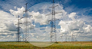 High voltage power lines in steppe covered with green and yellow grass under deep blue sky with heavy clouds.