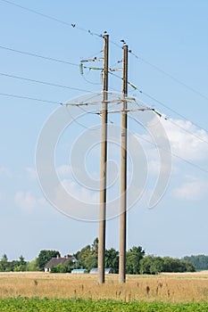 High-voltage power lines in wheat field meadow and blue sky background. High voltage electric transmission towers