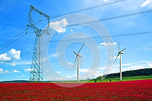 High voltage power lines with wind turbines in crimson clovers field.