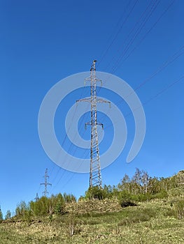 High voltage power stations standing in a field among green grass on a hill