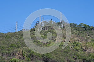 High voltage power transmission towers on top of a forested hill