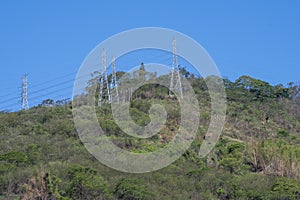 High voltage power transmission towers on top of a forested hill