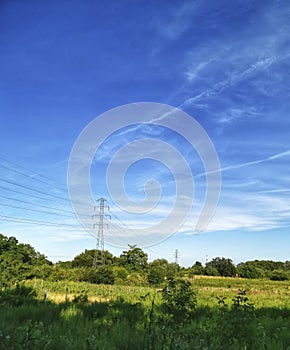 High voltage pylons and lines in a rural landscape against a blue sky. green country landscape on a sunny day.