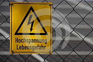 High voltage sign on a fence with solar panels in the background