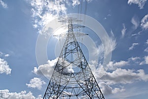 High voltage tower, Electric post and electric cable on the field in the countryside with white cloudy and blue sky background.