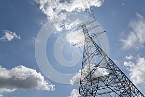 High voltage tower, Electric post and electric cable on the field in the countryside with white cloudy and blue sky background.