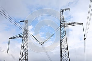 High-voltage towers with electricity transmission power lines against blue cloudy sky