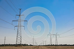 High voltage towers with electricity transmission power lines in field on sunny day