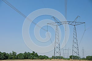 High voltage towers with electricity transmission power lines in field on sunny day