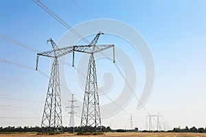 High voltage towers with electricity transmission power lines in field on sunny day