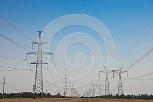 High voltage towers with electricity transmission power lines in field on sunny day