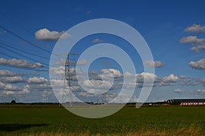 High voltage towers with electricity transmission power lines in field on sunny day