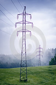 High voltage towers in a middle of forests and meadow. Electricity pylon with dark atmosphere in a nature. Rainy day. Power transm