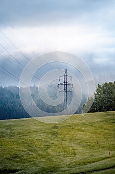 High voltage towers in a middle of forests and meadow. Electricity pylon with dark atmosphere in a nature. Rainy day. Power transm