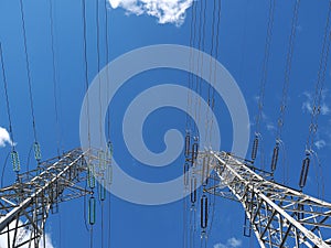 High voltage towers and wires against blue sky in park land