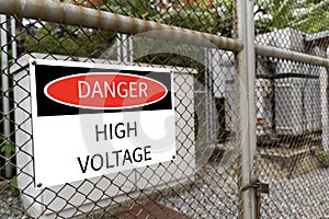 High-voltage transformer substation behind barbed-wire chain-link fence with Danger High Voltage sign