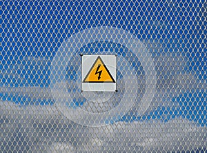 High voltage, warning sign, on chain link fence. Blue sky with fluffy clouds behind it