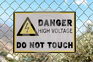 A high voltage warning sign on the fence on sky background
