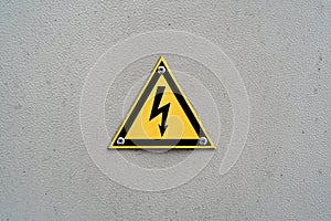 High voltage yellow triangle warning sign on gray metal wall