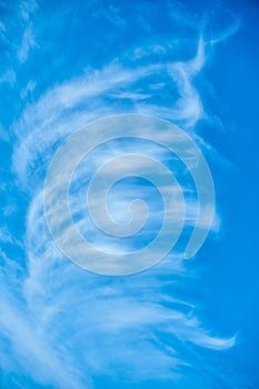 High white wispy cirrus clouds expanding by wind to cover deep navy blue sky in summer sunny day.