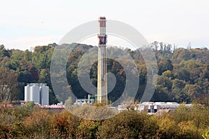 High wide concrete red and white rectangle industrial chimney rising high above industrial complex with new storage tanks