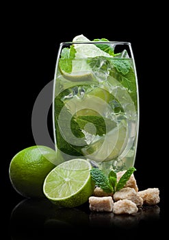 Highball glass of Mojito summer alcoholic cocktail with ice cubes mint and lime on black with cane sugar and limes