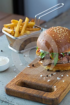 Highigh burger with french fries in small fry basket on concrete surface. Traditional American fastfood.