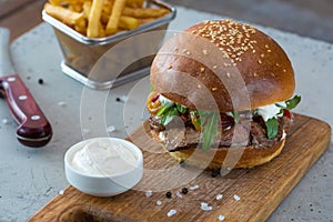 Highigh burger with french fries in small fry basket on concrete surface. Traditional American fastfood.