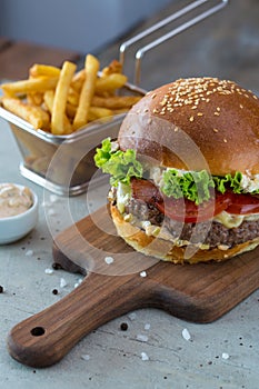 Highigh burger with french fries in small fry basket on concrete surface. Traditional American fastfood.