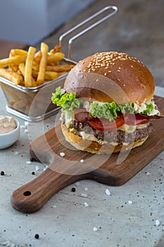 Highigh burger with french fries in small fry basket on concrete surface. Traditional American fastfood.