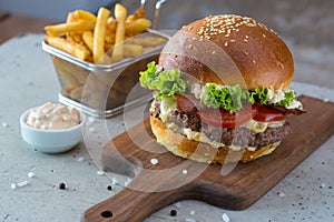 Highigh burger with french fries in small fry basket on concrete surface. Traditional American fastfood.