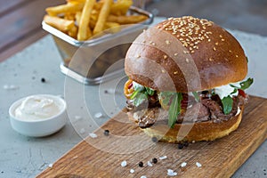 Highigh burger with french fries in small fry basket on concrete surface. Traditional American fastfood.