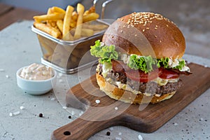 Highigh burger with french fries in small fry basket on concrete surface. Traditional American fastfood.