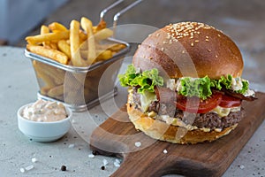 Highigh burger with french fries in small fry basket on concrete surface. Traditional American fastfood.