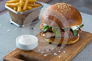 Highigh burger with french fries in small fry basket on concrete surface. Traditional American fastfood.