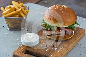 Highigh burger with french fries in small fry basket on concrete surface. Traditional American fastfood.