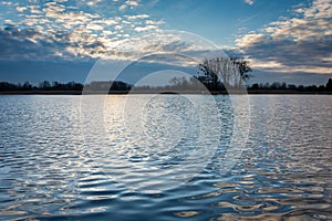 Highlighted clouds through the sun over a calm lake and reflection of clouds in waves