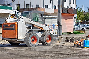 A highly manoeuvrable construction vehicle with a jackhammer attached is parked at a work site with a city street being repaired