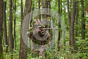 A highly skilled elite sniper, camouflaged in the dense forest, stealthily maneuvers through dangerous woodland terrain